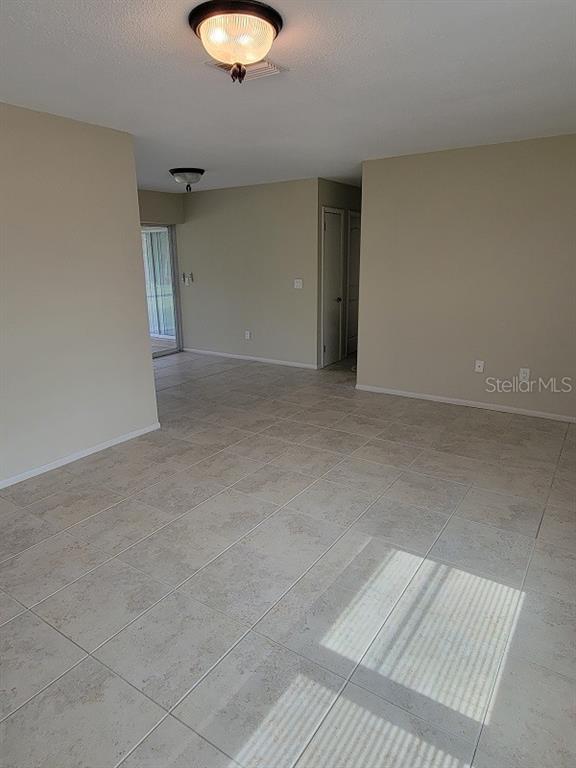 An empty room with beige walls, light-colored tile flooring, and two flush-mount ceiling lights — 474 HINTON STREET, PORT CHARLOTTE, FL