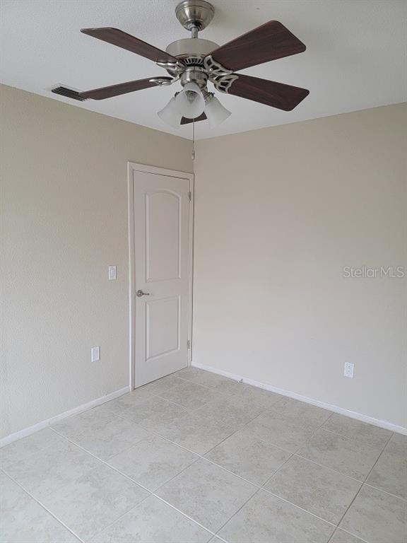 A room with light-colored tile flooring, beige walls, a ceiling fan, and a closed door — 474 HINTON STREET, PORT CHARLOTTE, FL