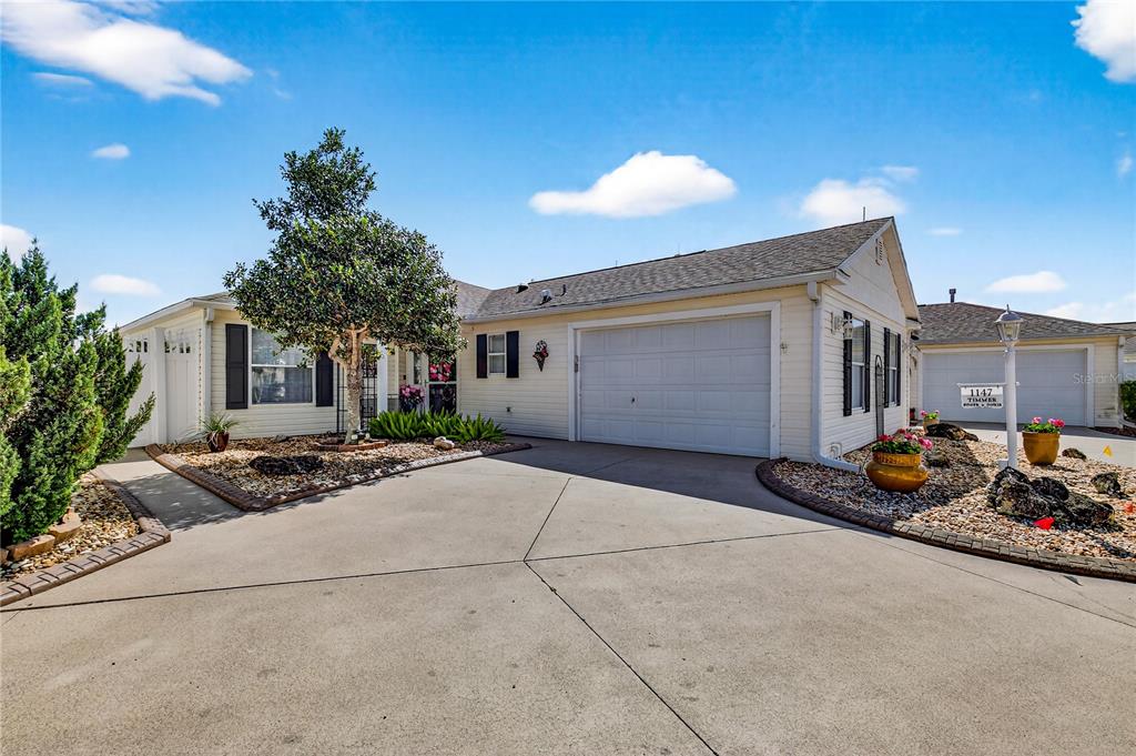 A single-story house with light siding, a two-car garage, and a landscaped front yard — 1147 ELIZABETH COURT, THE VILLAGES, FL