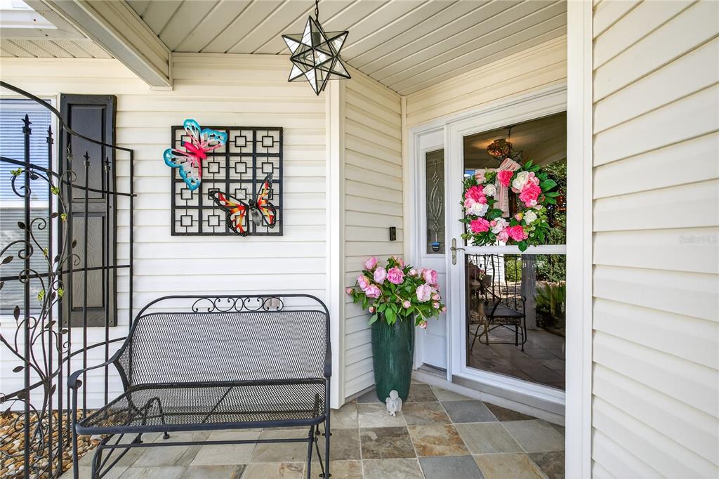A covered front porch features a metal bench, a decorative wall butterfly, and a floral wreath — 1147 ELIZABETH COURT, THE VILLAGES, FL