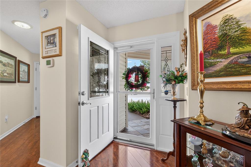 An entryway features a white front door, wood flooring, and a glass-topped console table — 1147 ELIZABETH COURT, THE VILLAGES, FL