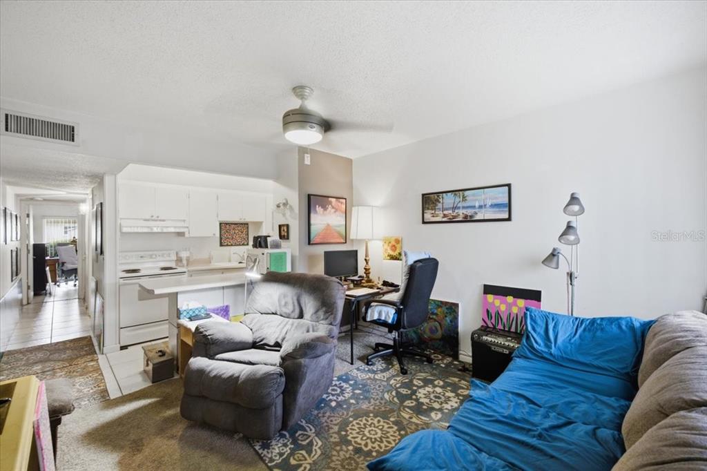 A living room with a recliner, desk, and sofa, opening into a kitchen area — 1235 S HIGHLAND AVENUE UNIT 5-102, CLEARWATER, FL