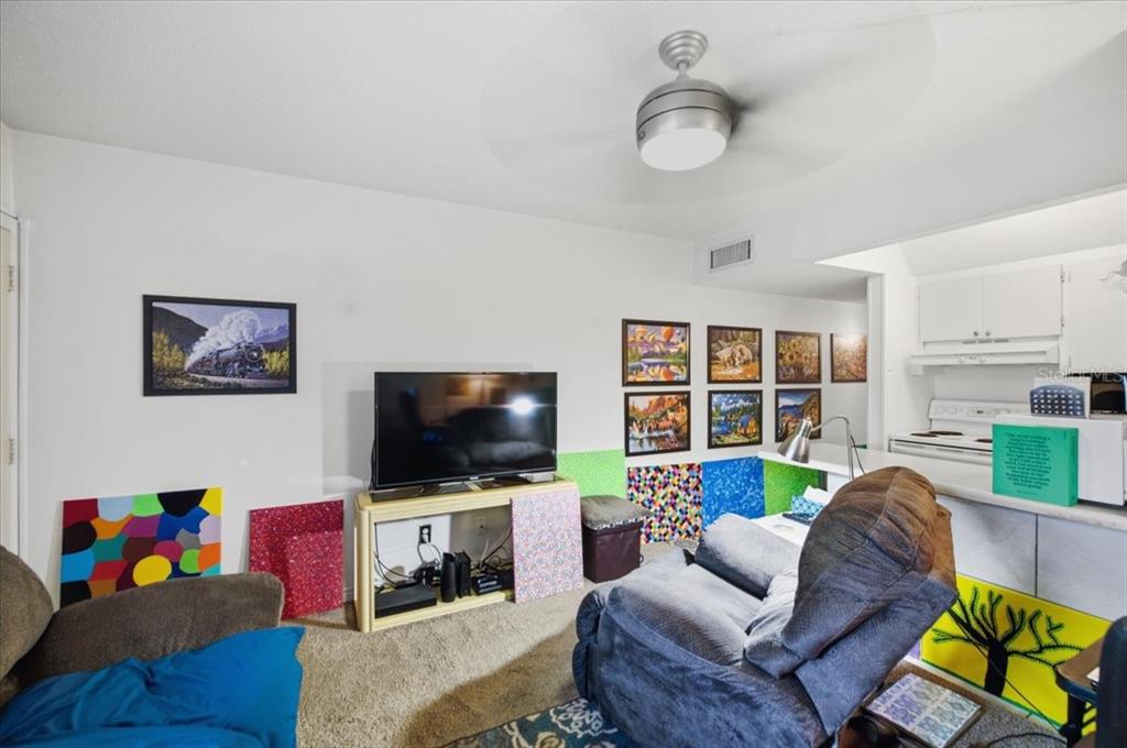 A living room features a television on a stand, a recliner, and various wall art — 1235 S HIGHLAND AVENUE UNIT 5-102, CLEARWATER, FL