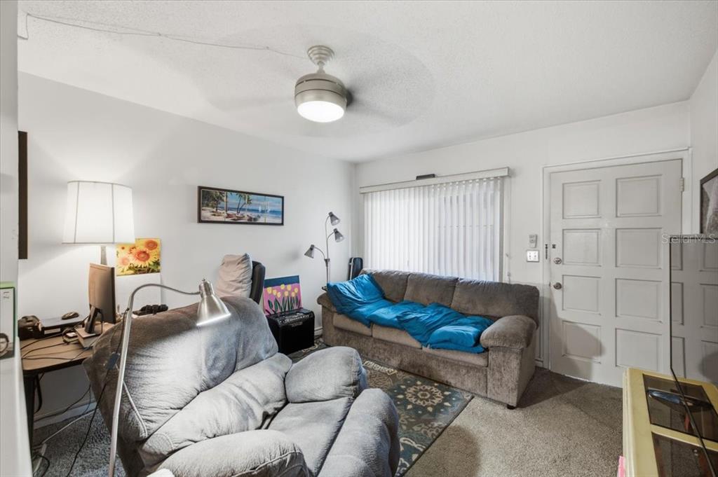 A living room features a gray recliner, a sofa with a blue blanket, and a desk — 1235 S HIGHLAND AVENUE UNIT 5-102, CLEARWATER, FL