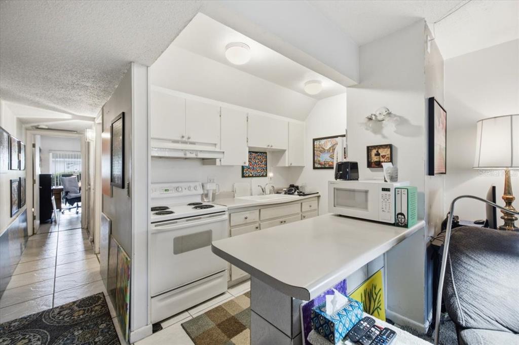 A kitchen features white cabinets, a white stove, and a breakfast bar with a microwave — 1235 S HIGHLAND AVENUE UNIT 5-102, CLEARWATER, FL