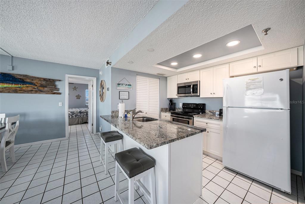 A kitchen with white cabinets, granite countertops, a breakfast bar, and white tile flooring — 19925 GULF BOULEVARD UNIT 407, INDIAN SHORES, FL