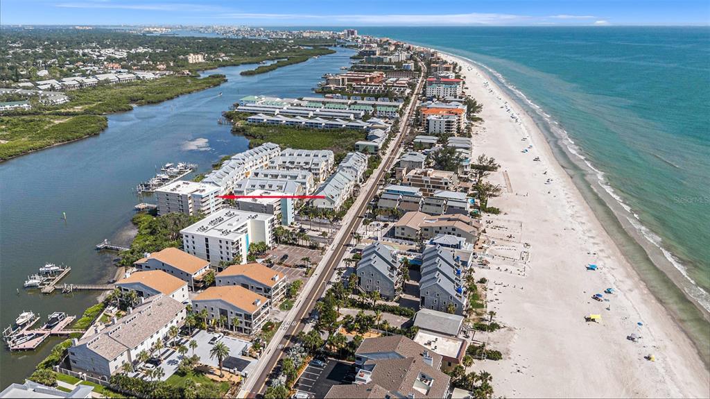 An aerial view shows a coastal residential complex situated between a waterway and the beach — 19925 GULF BOULEVARD UNIT 407, INDIAN SHORES, FL