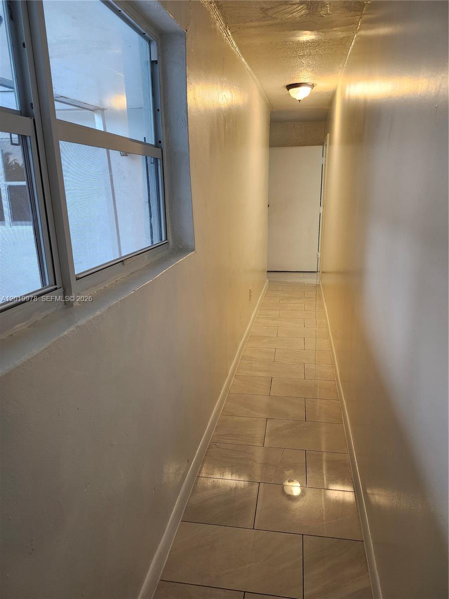 A narrow hallway features light-colored tile flooring, beige walls, and a window on the left — 551 NE 139th St # 551, North Miami FL 33161, NORTH MIAMI, FL
