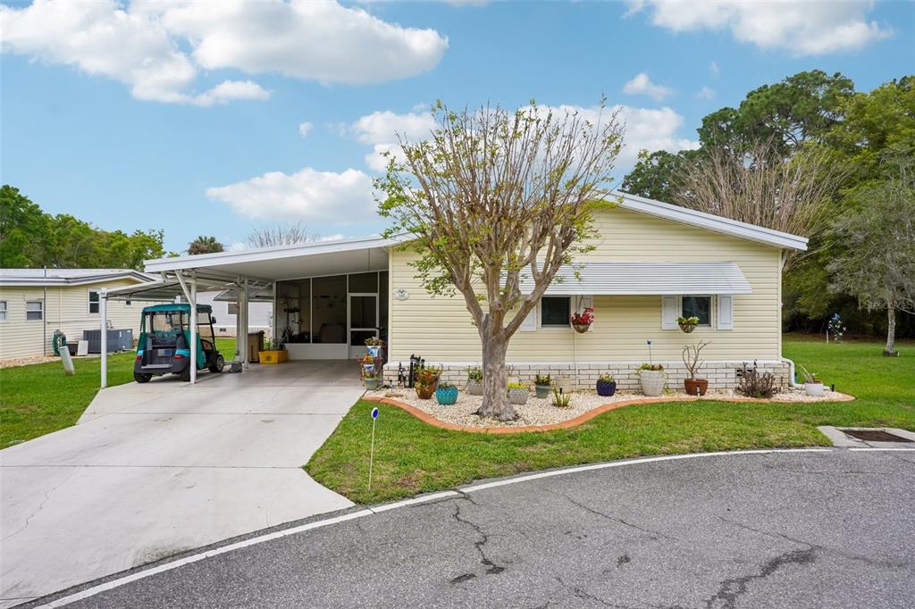 A yellow single-story mobile home features a carport, a paved driveway, and a landscaped yard — 122 TAMARISK WAY, LEESBURG, FL