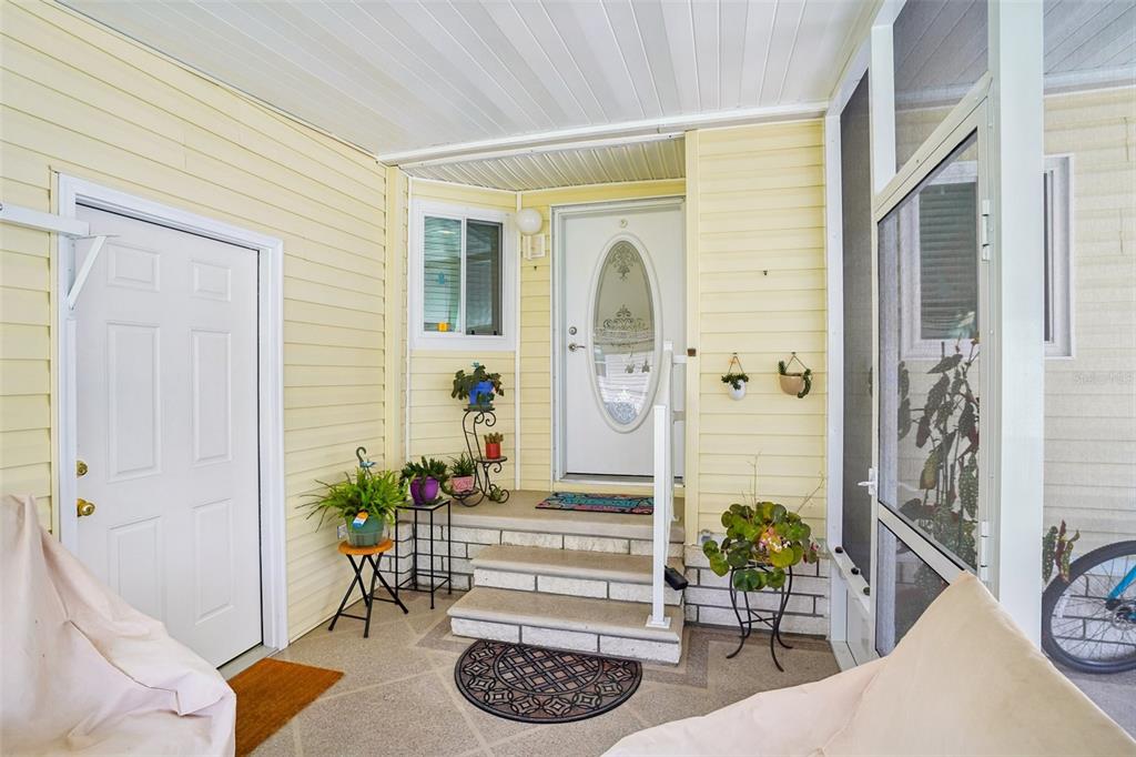 A covered porch features yellow siding, concrete steps leading to a front door, and potted plants — 122 TAMARISK WAY, LEESBURG, FL