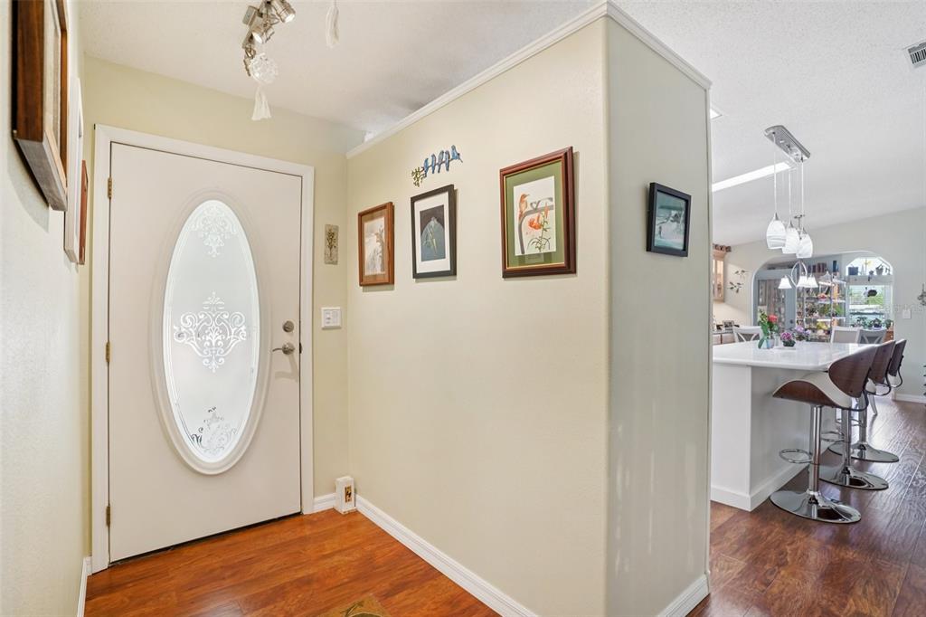 An entryway with a white front door, wood flooring, and a view into a kitchen — 122 TAMARISK WAY, LEESBURG, FL