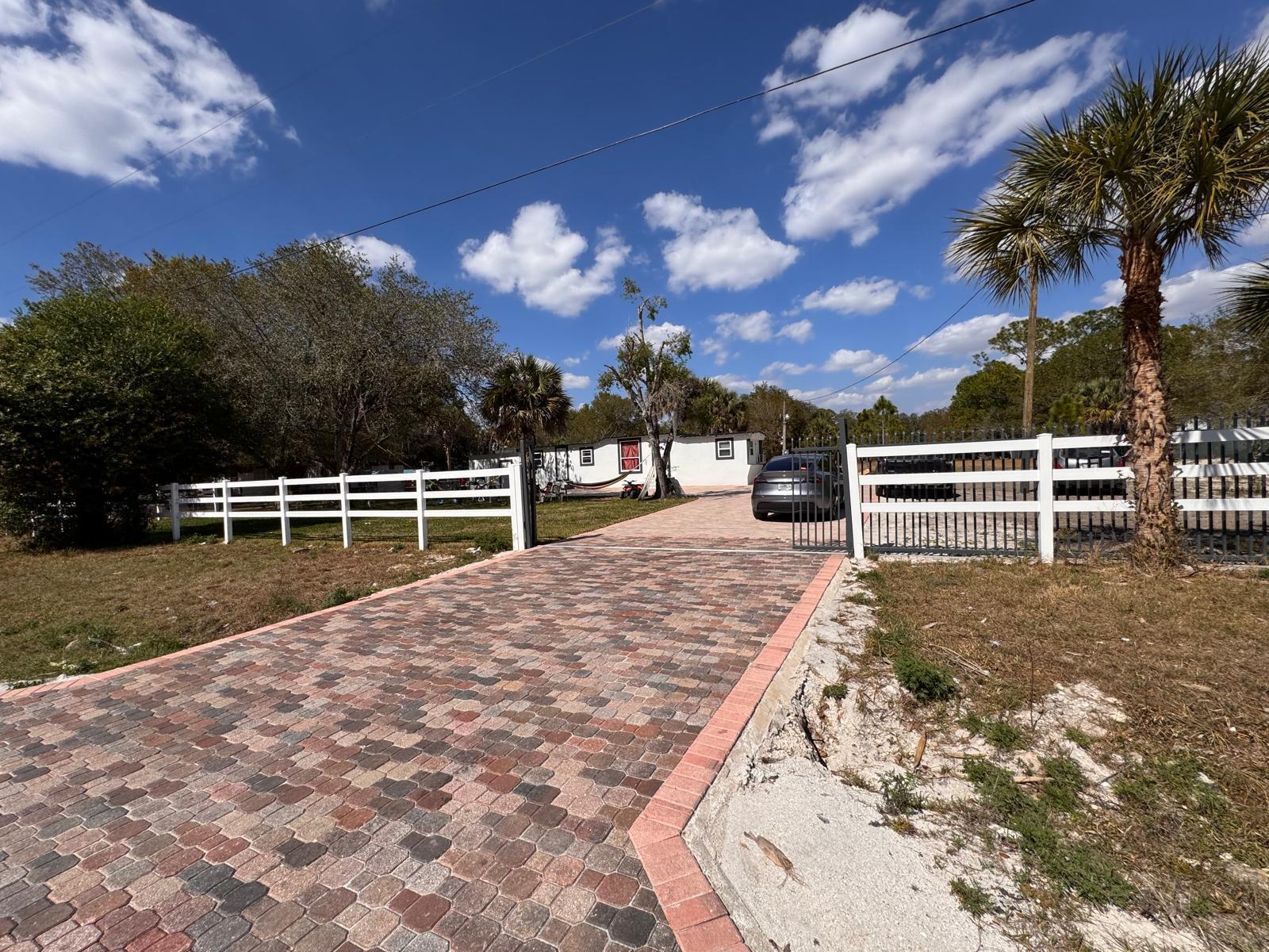 A paved driveway leads through a white fence and gate to a single-story house — 357 Hunting Club Avenue, Clewiston FL 33440, CLEWISTON, FL