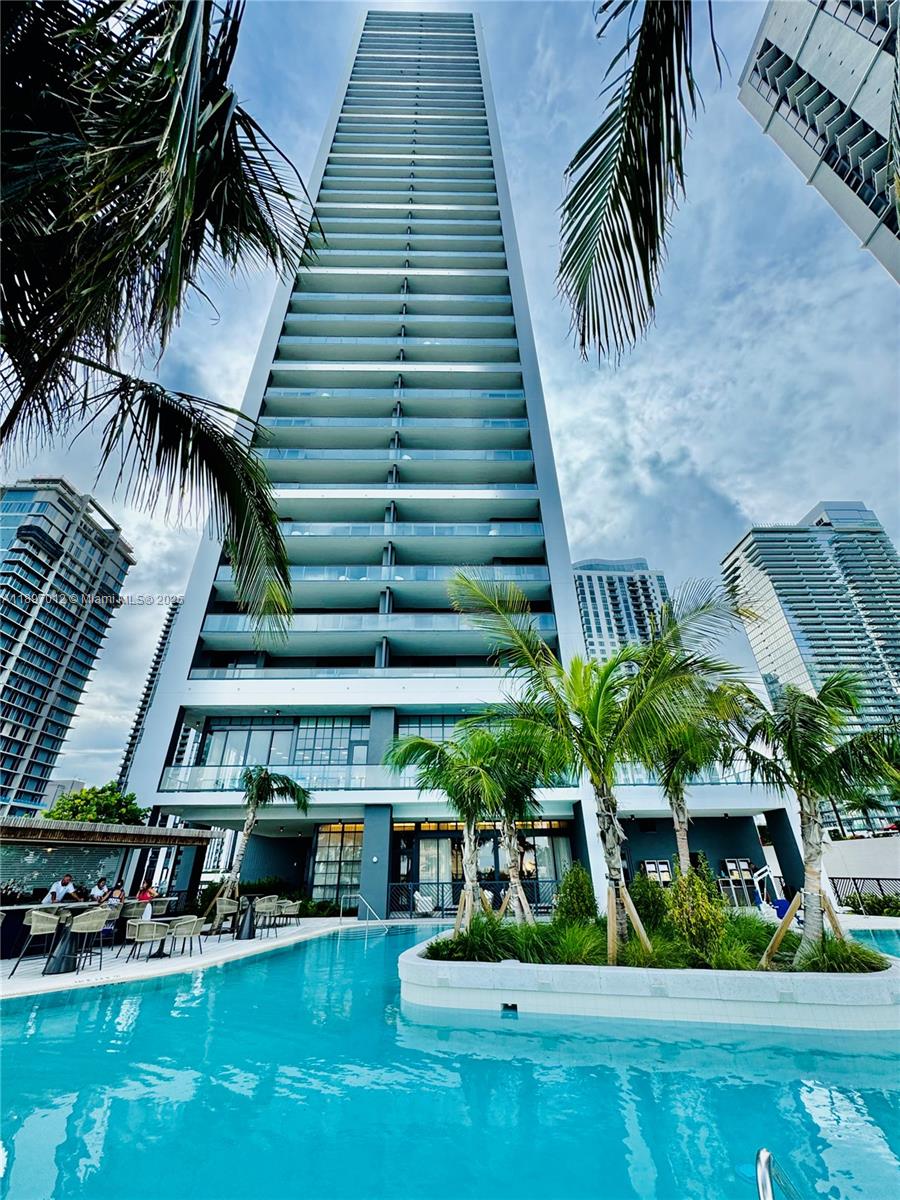 A tall residential skyscraper rises above a swimming pool with palm trees and lounge seating — 159 NE 6th St # 4314, Miami FL 33132, MIAMI, FL
