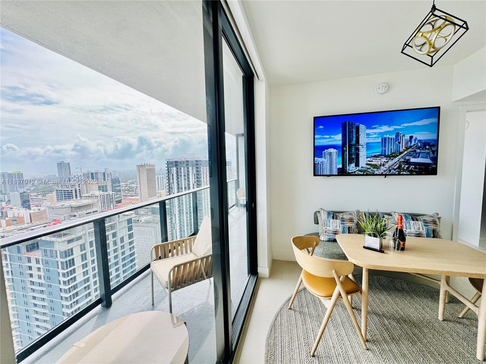 A dining area with a table and chairs overlooks a city balcony through sliding doors — 159 NE 6th St # 4314, Miami FL 33132, MIAMI, FL