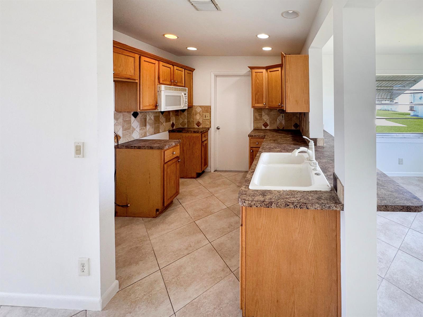 A kitchen features oak cabinets, laminate countertops, a white double sink, and tiled flooring — 514 SW 20th Street, Boynton Beach FL 33426, BOYNTON BEACH, FL