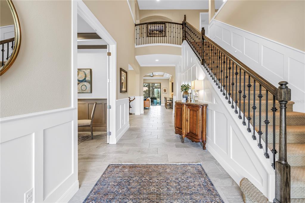 A foyer features a staircase with iron railings, tile flooring, and a view into a hallway — 6237 SIGNATURE POINTE LANE, BRADENTON, FL
