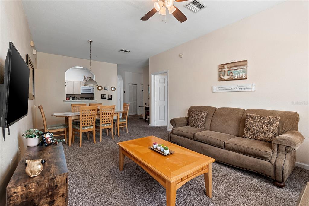 A living room with a brown sofa, wooden coffee table, and an adjacent dining area — 8103 COCONUT PALM WAY UNIT 205, KISSIMMEE, FL