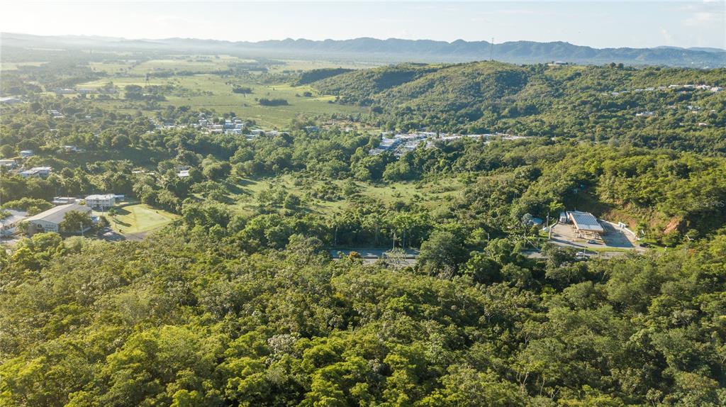 An aerial view shows a lush, hilly landscape with a gas station and scattered residential buildings — 100 PUERTO RICO, CABO ROJO, PR