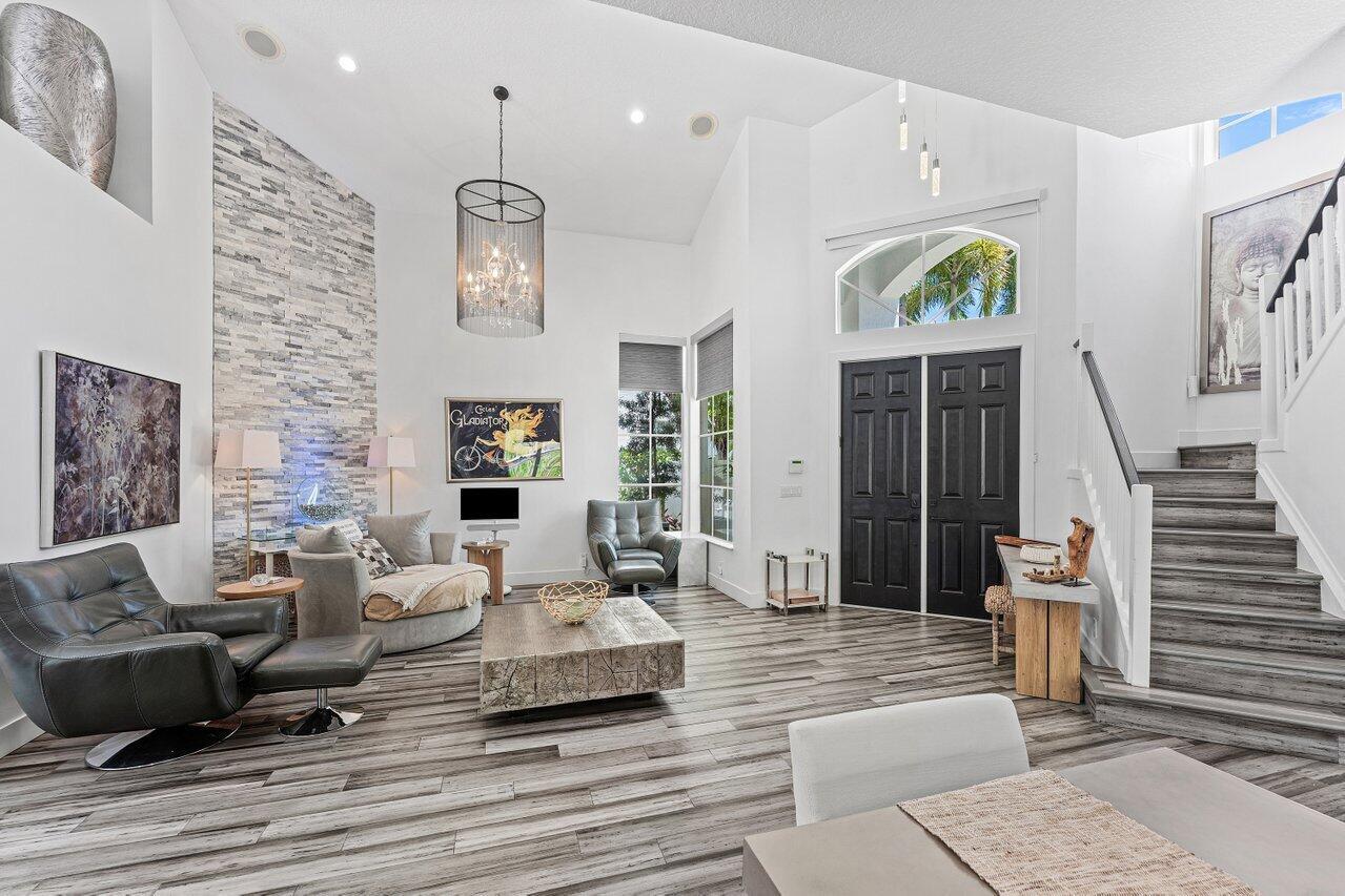 A bright living room features a stone accent wall, wood-look flooring, and a grand staircase — 3395 NW 53rd Circle, Boca Raton FL 33496, BOCA RATON, FL