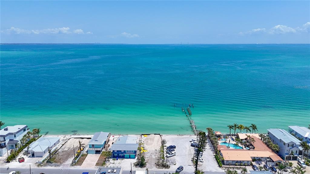 An aerial view shows a coastal neighborhood with houses, a sandy beach, and a wooden pier — 873 N SHORE DRIVE, ANNA MARIA, FL