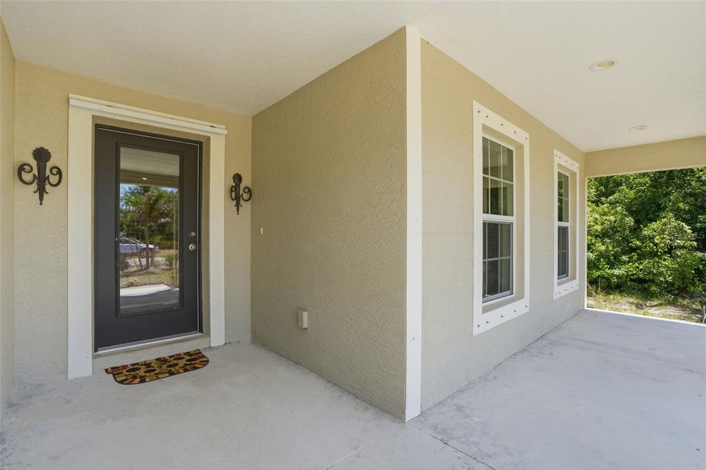 A covered front porch features a dark glass-paneled door, two windows, and beige stucco walls — 126 GREEN PINE PARK, ROTONDA WEST, FL