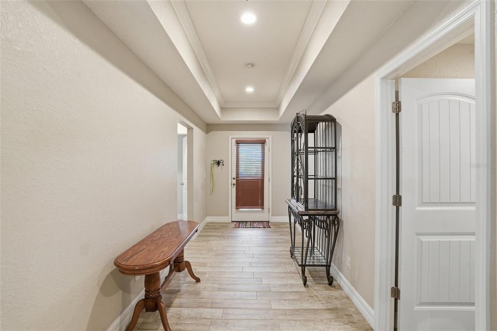 A hallway features a tray ceiling, tile flooring, a wooden console table, and a metal shelf — 126 GREEN PINE PARK, ROTONDA WEST, FL