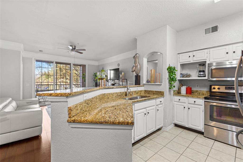 A kitchen with white cabinets, granite countertops, and stainless steel appliances overlooks a living area — 3480 SOHO STREET UNIT 201, ORLANDO, FL
