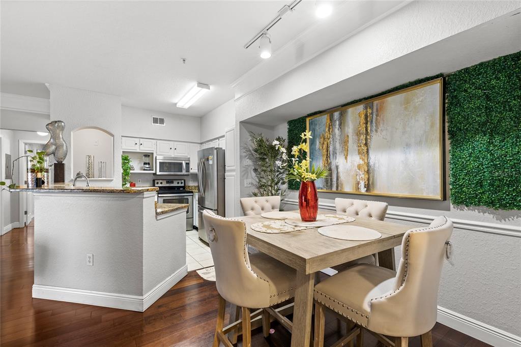 A dining area with a wooden table, upholstered chairs, and a large abstract wall art — 3480 SOHO STREET UNIT 201, ORLANDO, FL