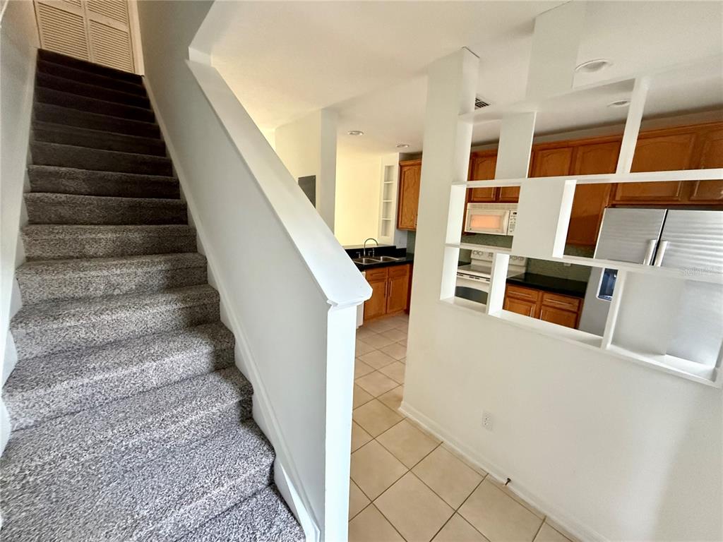 A carpeted staircase leads upward next to a kitchen with wood cabinets and tile flooring — 3549 WILSHIRE WAY ROAD UNIT 3549, ORLANDO, FL