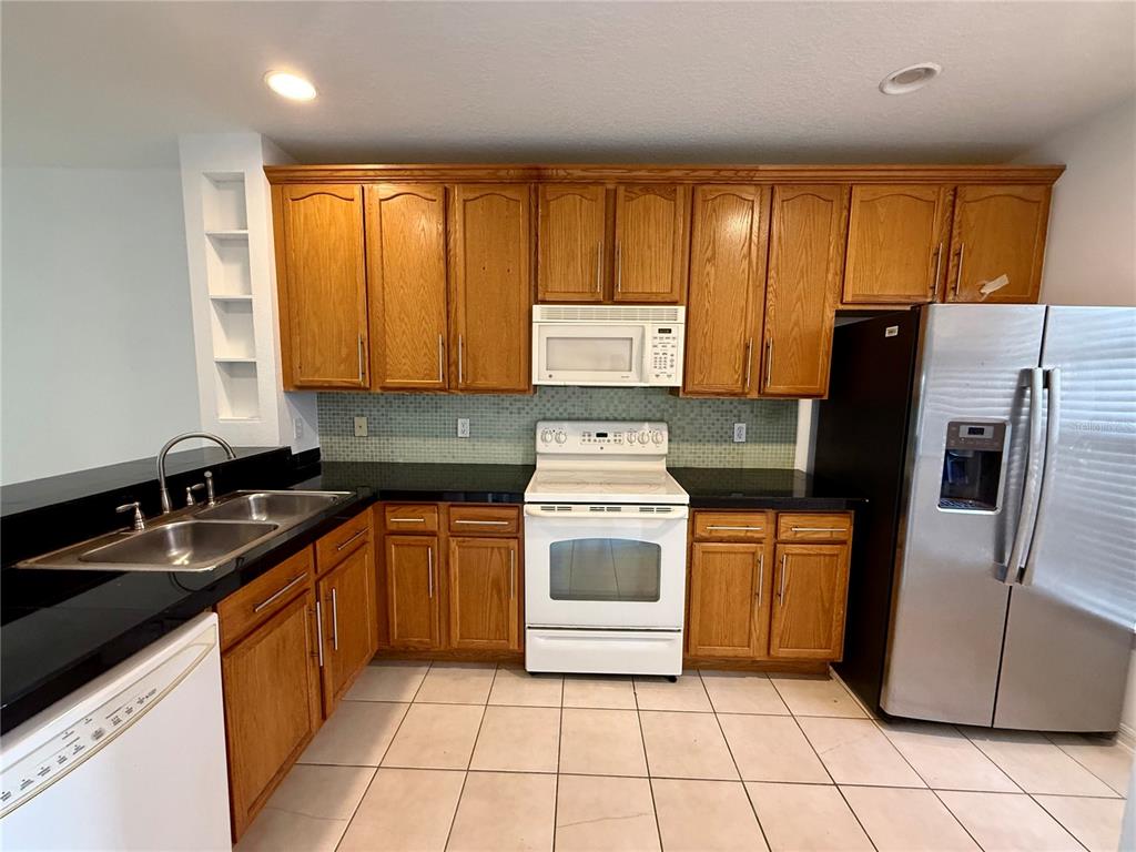 A kitchen features oak cabinets, black countertops, white appliances, and light-colored floor tiles — 3549 WILSHIRE WAY ROAD UNIT 3549, ORLANDO, FL