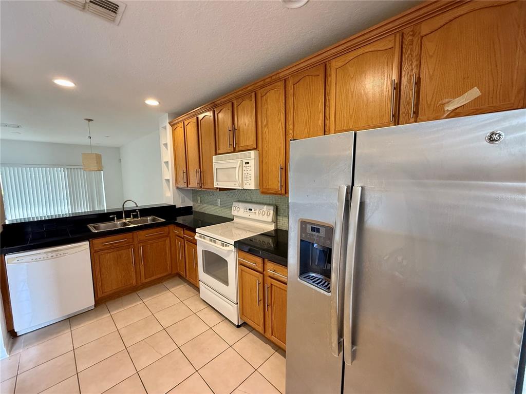 A kitchen features oak cabinets, black countertops, a white stove, and a stainless steel refrigerator — 3549 WILSHIRE WAY ROAD UNIT 3549, ORLANDO, FL