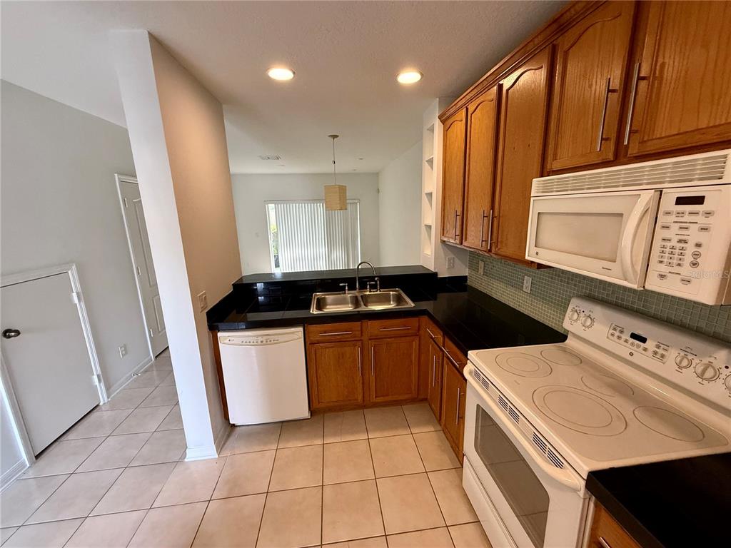 A kitchen features wood cabinets, black countertops, a white stove, and a white dishwasher — 3549 WILSHIRE WAY ROAD UNIT 3549, ORLANDO, FL