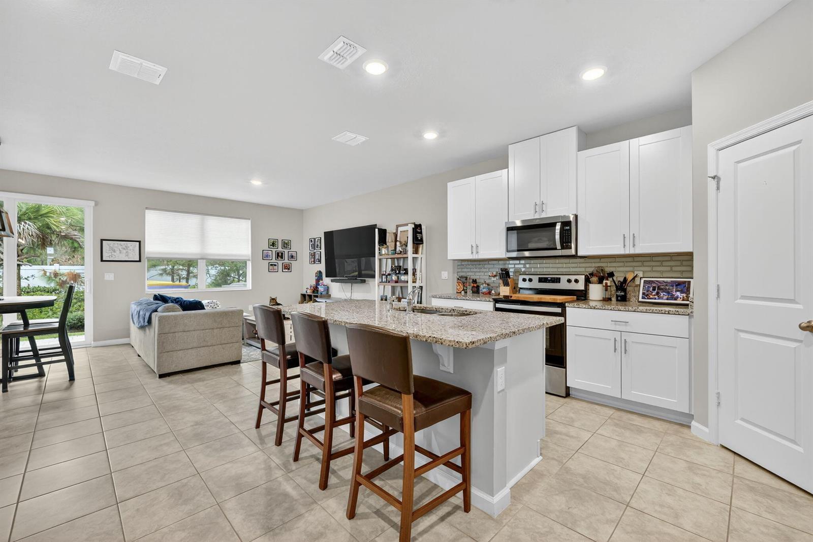 A kitchen with white cabinets, granite countertops, and a breakfast bar faces a living area — 5672 SE Edgewater Circle, Stuart FL 34997, STUART, FL