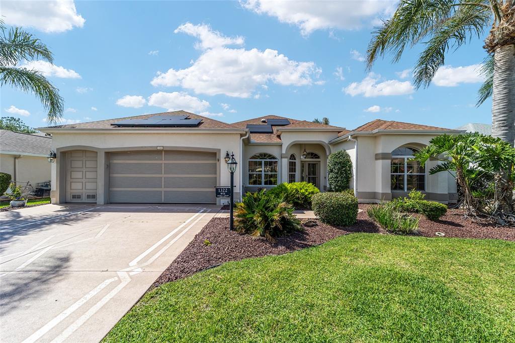 A single-story house features a two-car garage, solar panels, and a landscaped front yard — 1322 AUGUSTINE DRIVE, THE VILLAGES, FL