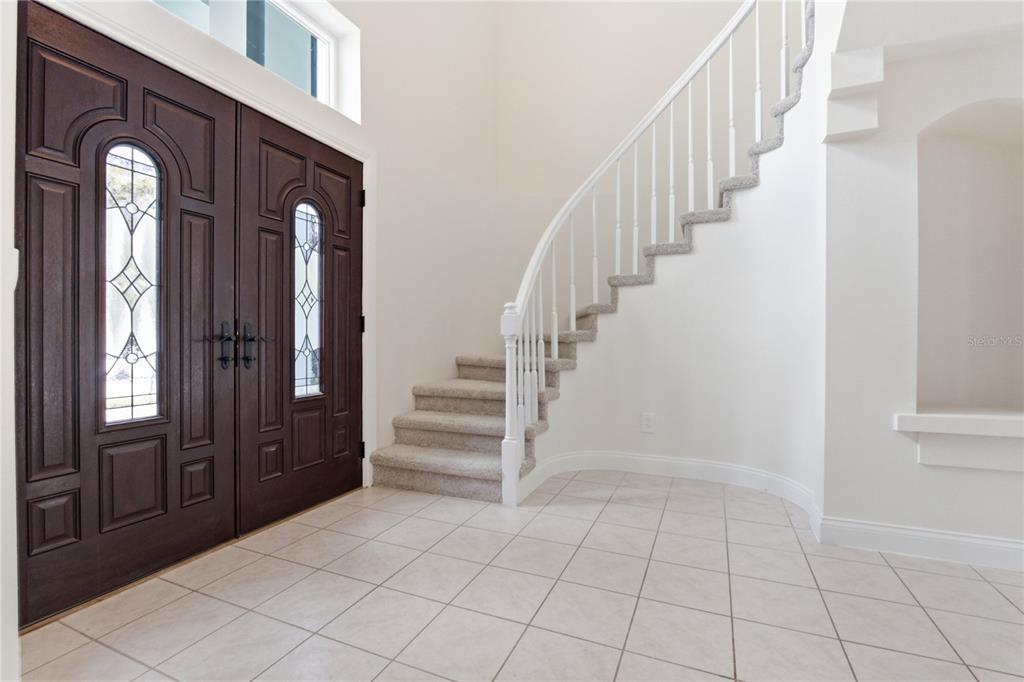 An entryway features a tiled floor, a curved staircase with carpet, and double wooden doors — 1307 HAMPSTEAD TERRACE, OVIEDO, FL