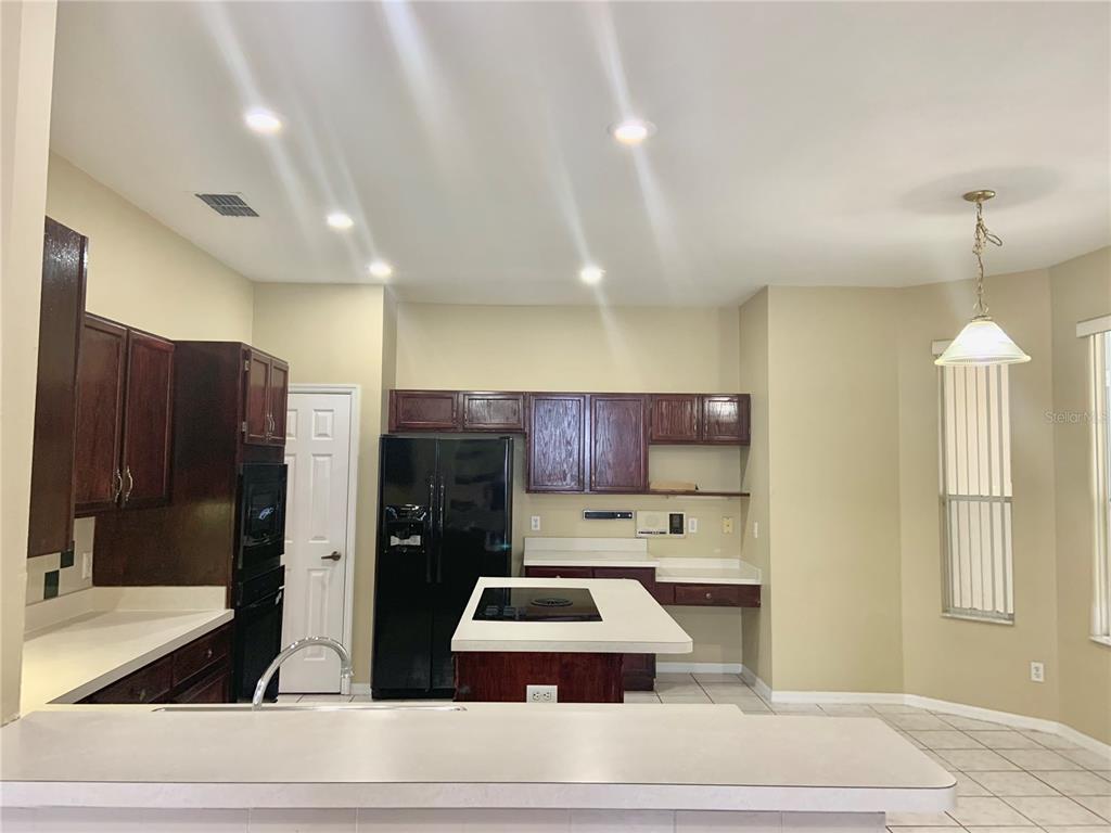 A kitchen features dark wood cabinets, black appliances, a central island, and light-colored countertops — 3878 KINGSTON OAKS COVE, OVIEDO, FL
