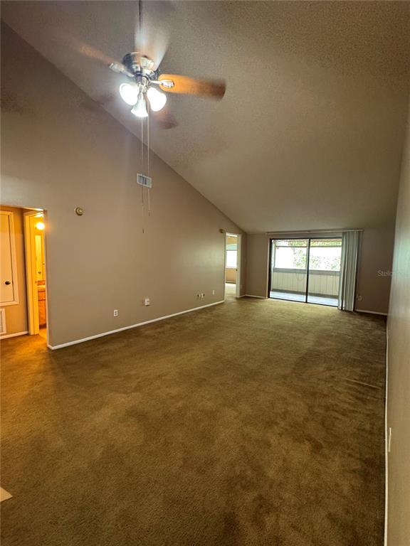 A spacious living room with tan carpet, a vaulted ceiling, and a sliding glass door — 5359 VINELAND ROAD UNIT 2E, ORLANDO, FL
