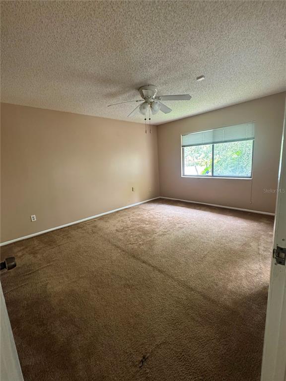 An empty bedroom features beige walls, brown carpeting, a ceiling fan, and a single window — 5359 VINELAND ROAD UNIT 2E, ORLANDO, FL