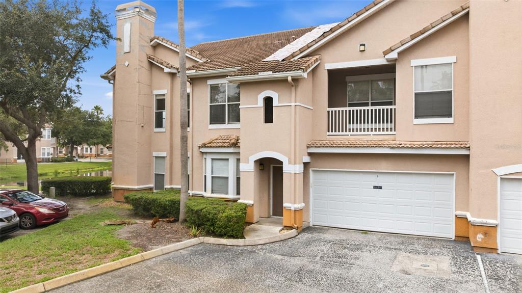 A two-story tan stucco townhouse features a white garage door and a second-floor balcony — 10436 VILLA VIEW CIRCLE, TAMPA, FL