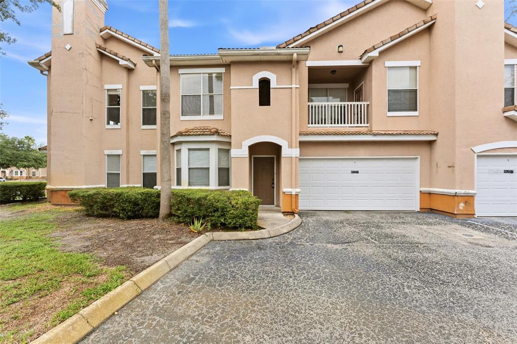 A two-story tan stucco townhouse with a white garage door and a small balcony — 10436 VILLA VIEW CIRCLE, TAMPA, FL