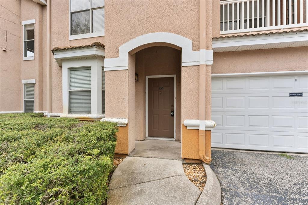 A tan stucco townhouse exterior features a brown front door, a garage, and landscaping — 10436 VILLA VIEW CIRCLE, TAMPA, FL