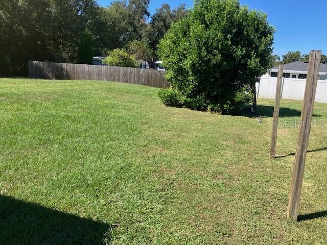 A grassy backyard features a wooden fence, a large tree, and two wooden posts — 5527 GAUR LANE, LAKELAND, FL