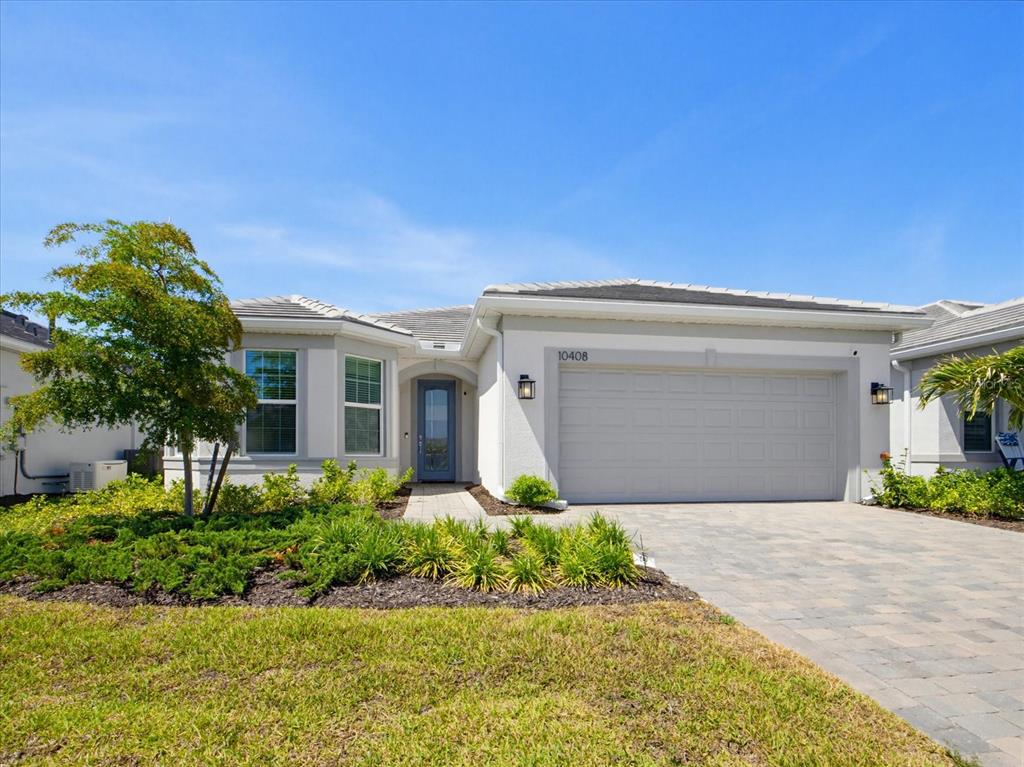 A single-story house with a gray garage, blue front door, and landscaped front yard — 10408 SEA BREEZE RIDGE DRIVE, ENGLEWOOD, FL