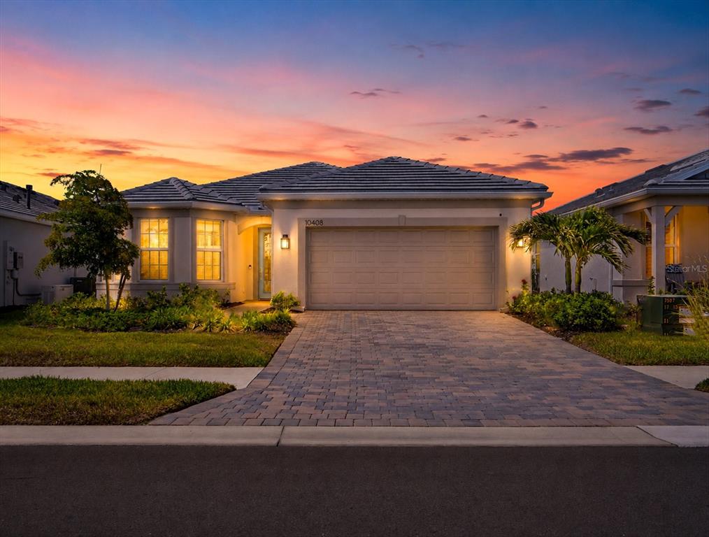A single-story house with a paved driveway and a two-car garage at sunset — 10408 SEA BREEZE RIDGE DRIVE, ENGLEWOOD, FL