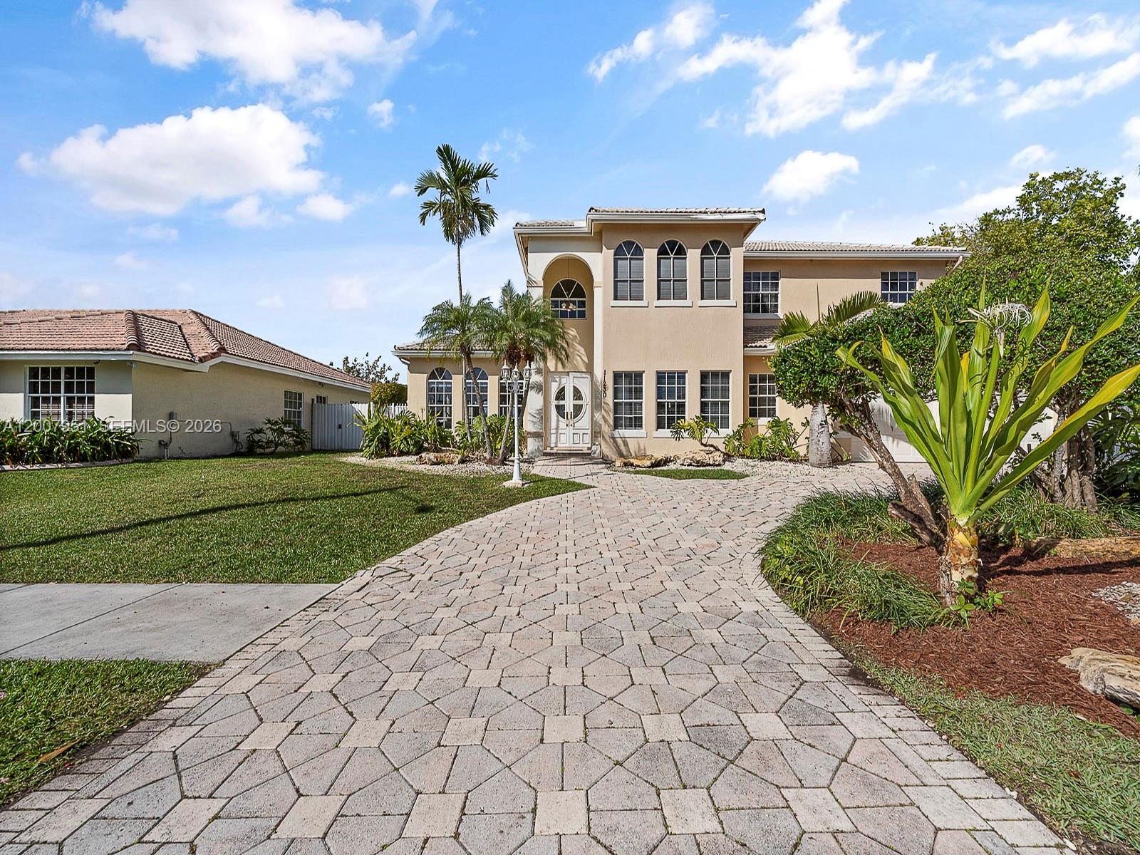 A two-story beige house with a paved driveway and arched windows under a blue sky — 11230 SW 156th Ave, Miami FL 33196, MIAMI, FL