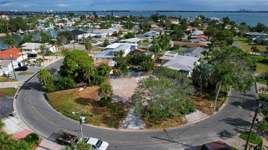 An aerial view shows a vacant residential lot situated on a curved street near water — 3615 BELLE VISTA DRIVE E, ST PETE BEACH, FL
