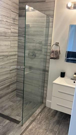 A modern bathroom features a glass-enclosed walk-in shower with gray wood-look tile and a vanity — MIAMI BEACH, FL