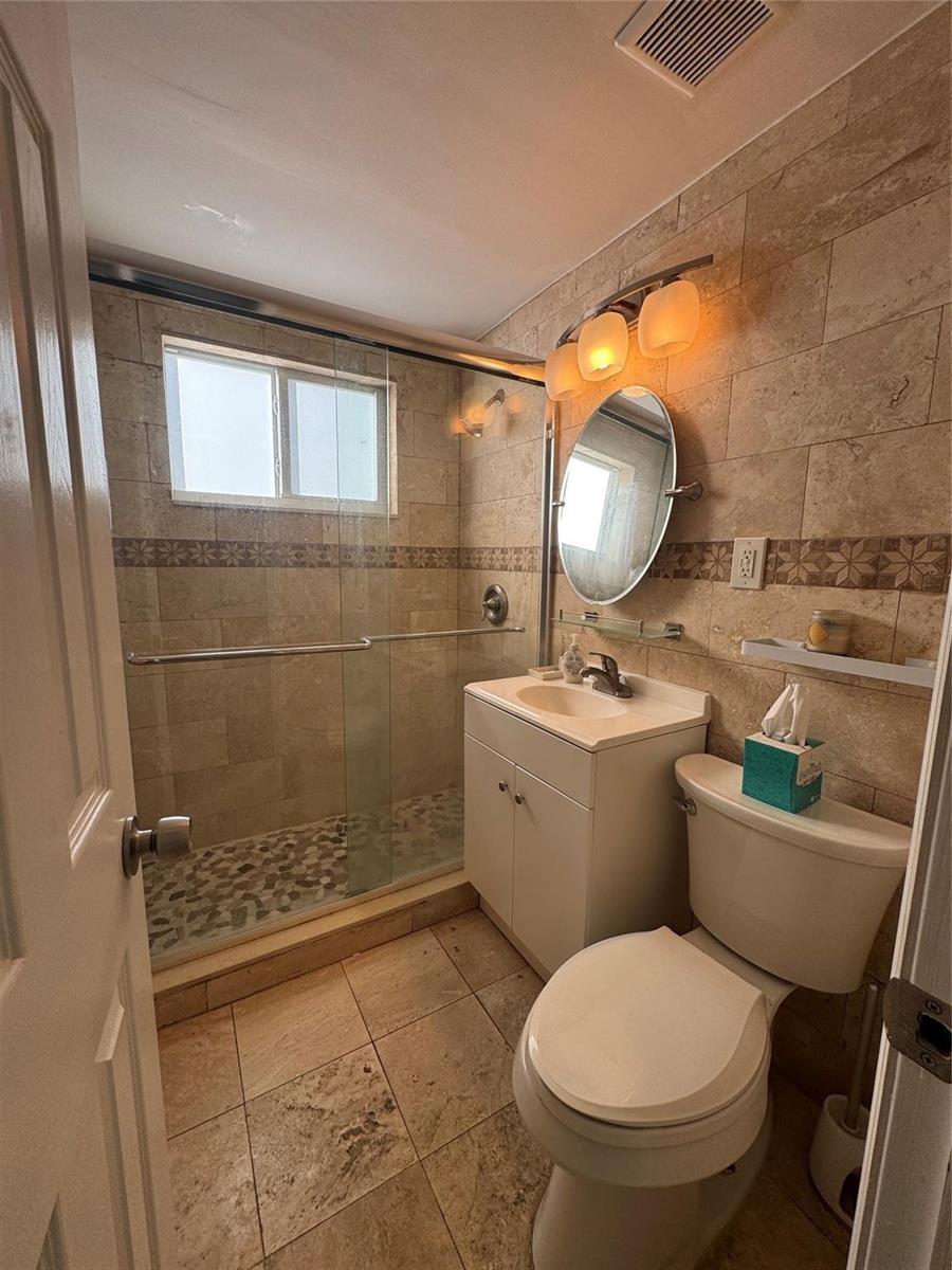 A bathroom features a glass-enclosed shower, a white vanity, a toilet, and beige tile walls — 323 Monroe Street # 2, Hollywood FL 33019, HOLLYWOOD, FL