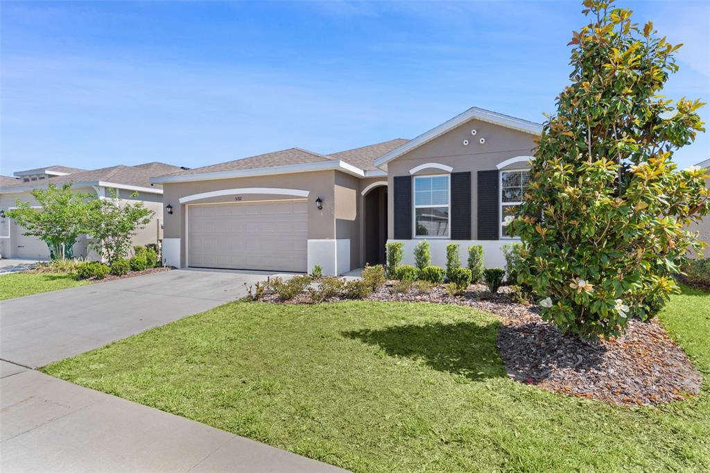 A single-story house with a beige exterior, a two-car garage, and a front yard — 5092 STOKES WAY, WILDWOOD, FL