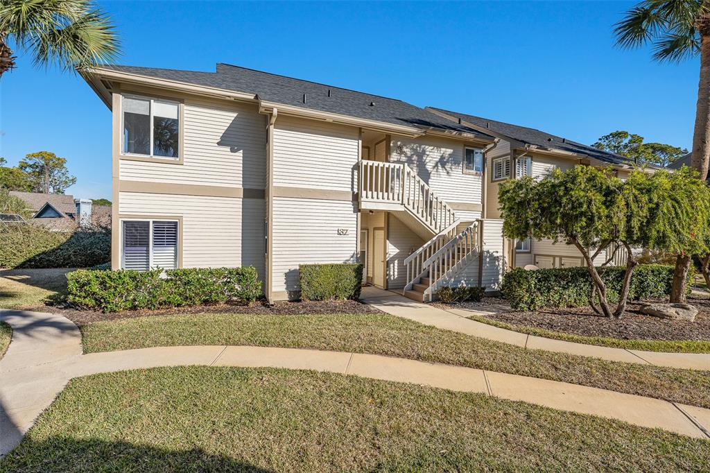 A two-story apartment building with beige siding, a staircase, and a landscaped front lawn — 39 MAGNOLIA DRIVE S UNIT 39, ORMOND BEACH, FL